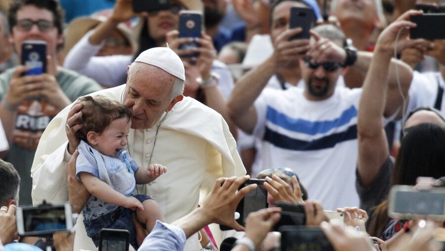 Papst Franziskus küsst bei der Generalaudienz ein kleines Kind. / © Riccardo De Luca (dpa)