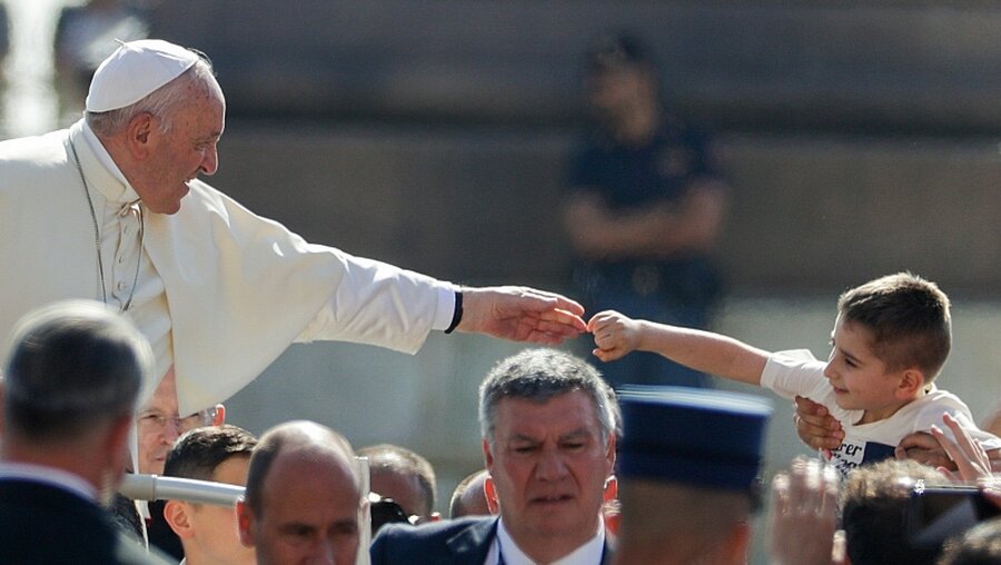 Papst Franziskus streckt die Hand zu einem Kind aus / © Andrew Medichini (dpa)