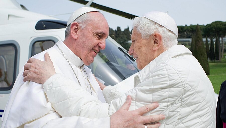 Papst Franziskus begrüßt den emeritierten Papst Benedit XVI.  / © OSSERVATORE ROMANO/dpa (dpa)