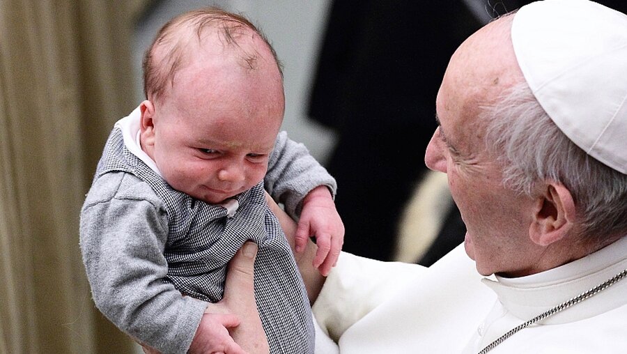 Papst Franziskus hat ein Baby im Arm.  / © Evandro Inetti (dpa)