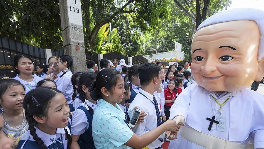 Schulkinder begrüßen einen Mann mit einer riesigen Maske vom Papst Franziskus vor der Botschaft der Apostolischen Nuntiatur des Heiligen Stuhls / © Manish Swarup (dpa)