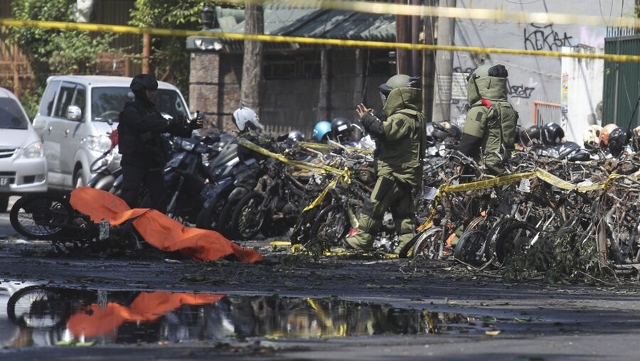 In Schutzanzügen untersuchen Polizei-Beamte nach einer Explosion nahe einer christlichen Kirche abgestellte Motorroller. / © Trisnadi/AP (dpa)