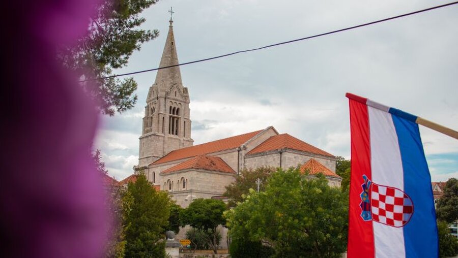 Symbolbild: Kirche in Kroatien. Vor der Kirche von Selca weht die kroatische Flagge. / © Antonio Batinic (shutterstock)