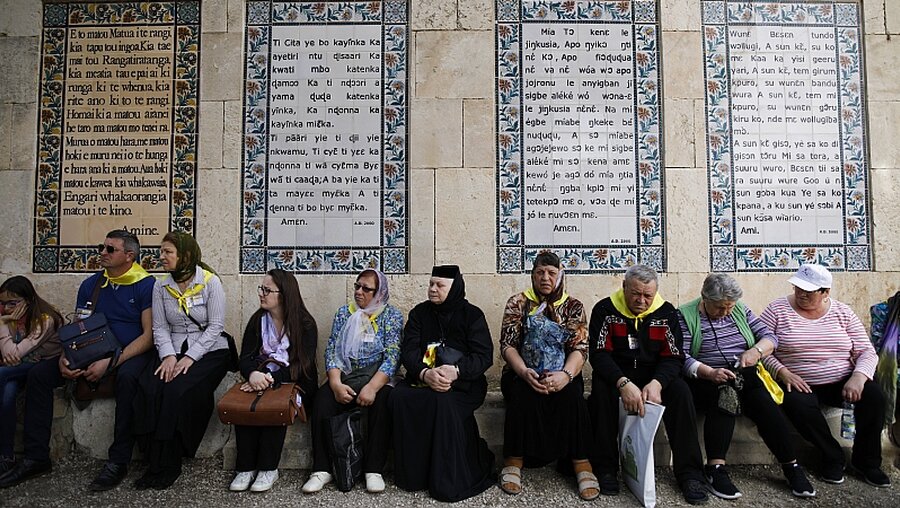 Touristen sitzen vor Keramiktafeln, auf denen das Vaterunser in verschiedenen Sprachen steht, in der Paternosterkirche in Jerusalem / © Corinna Kern (KNA)