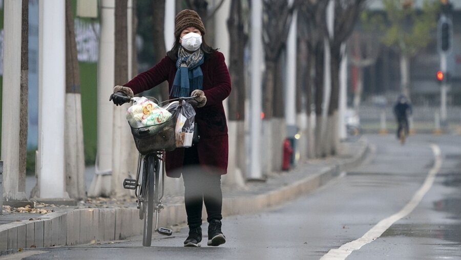  Wuhan: Eine Frau mit Mundschutz schiebt ihr Fahrrad auf einer Straße / © Xiong Qi (dpa)