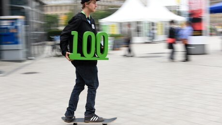 Skateboardfahrer mit einer grünen 100 in der Hand, während des 100. Deutschen Katholikentag. (KNA)