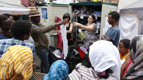 Afrikanische Flüchtlinge erhalten von Ehrenamtlichen Kleidung, in einer Straße, in der Flüchtlinge vorübergehend in Zelten leben, am 14. Juli 2016 in Rom. (KNA)