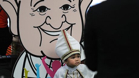  Ein als Papst verkleidetes Kind steht vor einer Comicfigur von Papst Franziskus im Saint Louis Hospital / © Manish Swarup (dpa)