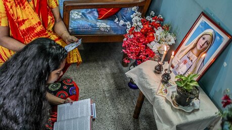 Ein Mädchen in Dhaka sitzt vor einem dekorierten Tisch mit Heiligenbildern. / © Turjoy Chowdhury (KNA)