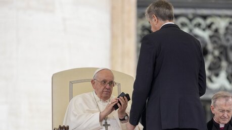 Papst Franziskus gibt am Ende eines Anrufs, den er während seiner wöchentlichen Generalaudienz auf dem Petersplatz im Vatikan erhielt, ein Handy zurück / © Andrew Medichini/AP (dpa)