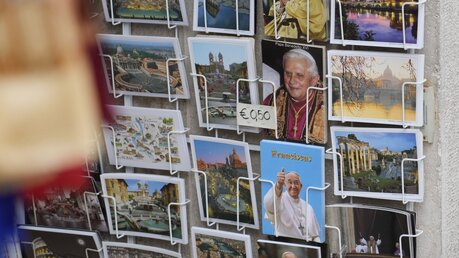 Im Vatikan werden Postkarten von Benedikt XVI. und Papst Franziskus verkauft. In Altötting in Bayern gibt es sogar Spielfiguren des Verstorbenen zu kaufen / © Gregorio Borgia (dpa)
