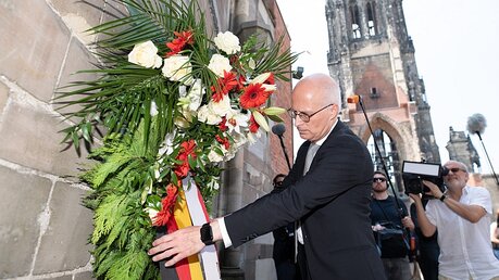 Peter Tschentscher (SPD), Erster Bürgermeister von Hamburg, richtet die Schleife eines Kranzes an den Ruinen der St. Nikolai-Kirche / © Daniel Reinhardt (dpa)