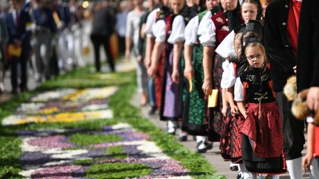 Trachtenträger laufen an Fronleichnam während der Prozession an einem Blumenteppich vorbei / © Patrick Seeger (dpa)