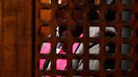 Beichte: Blick durch ein Holzgitter auf einen Priester mit violetter Stola in einem Beichtstuhl / © Harald Oppitz (KNA)