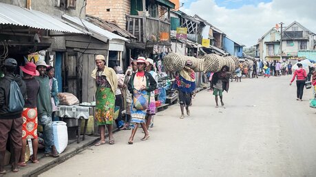 Menschen auf einer Straße, manche, darunter Frauen, tragen Säcke mit Braunkohle, am 16. Februar 2023 in Ambatolampy (Madagaskar). / © Alexander Brüggemann (KNA)