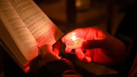 Schulgottesdienst: Ein Teilnehmer leuchtet mit einer Opferkerze auf das Liedblatt bei einem Wortgottesdienst / © Harald Oppitz (KNA)