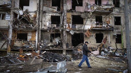 Ein Ukrainer geht an einem Gebäude vorbei, das nach einem Raketenangriff zerstört ist / © Emilio Morenatti (dpa)