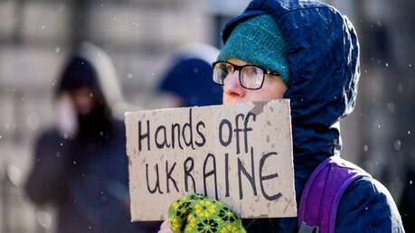 Eine Demonstrantin hält ein Schild mit der Aufschrift "Hands off Ukraine" (Hände weg von der Ukraine) / © Jane Barlow (dpa)