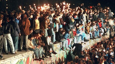 30 Jahre Mauerfall: Jubelnde Menschen sitzen mit Wunderkerzen auf der Berliner Mauer (dpa)