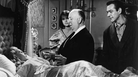 Alfred Hitchcock (M.) bei Dreharbeiten zu dem Film "Marnie" von 1964 / © akg-images GmbH (epd)