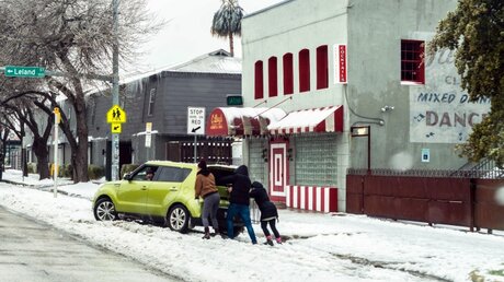 Austin, Texas: Menschen versuchen an einer Straße ein Auto aus dem Schnee zu schieben. / © Sandra Dahdah/ZUMA Wire (dpa)