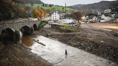 Blick auf Schuld an der Ahr nach der Flutkatastrophe. Hilfskräfte waten durch den Fluss neben einer Brücke / © Julia Steinbrecht (KNA)