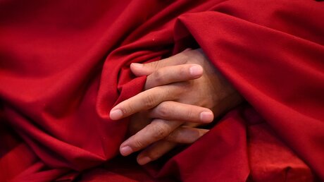 Die Hände eines buddhistischen Mönchs schauen aus seiner roten Kutte heraus / © Harald Oppitz (KNA)