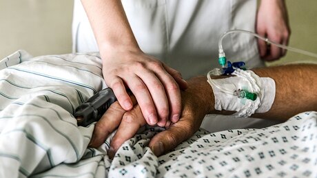 Die Hand einer Pflegerin liegt auf dem Handrücken eines Patienten auf der Intensivstation im Cura Krankenhaus Bad Honnef. / ©  Harald Oppitz (KNA)
