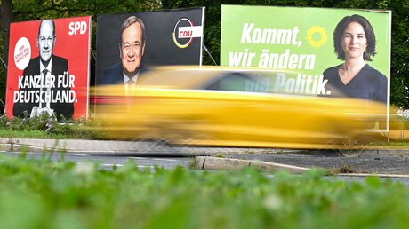 Ein Auto fährt an Wahlplakaten mit den Spitzenkandidaten Olaf Scholz, Armin Laschet und Annalena Baerbock vorbei. / © Arne Dedert (dpa)