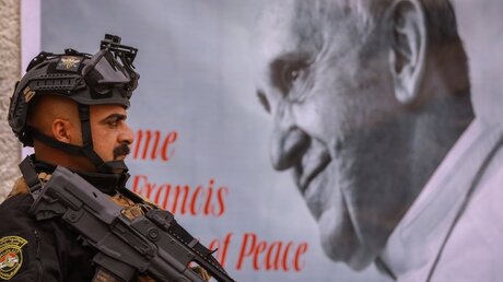 Ein bewaffneter Polizist steht an einer Kirche neben einem Bild des Papstes inmitten einer Sicherheitskontrolle / © Ameer Al Mohammedaw (dpa)