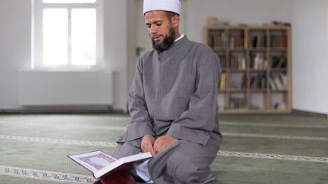 Ein Imam der Moschee am Islamischen Zentrum Dresden hält den Koran in der Hand. Zum Tag der offenen Moschee am 3. Oktober lädt das Zentrum interessierte Bürgerinnen und Bürger zum Besuch ein. / © Monika Skolimowska (dpa)