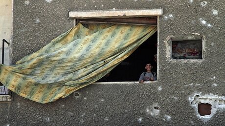 Ein Junge blickt aus einem Fenster in der zerstörten Stadt Duma. / © Hummam Sheikh Ali (dpa)