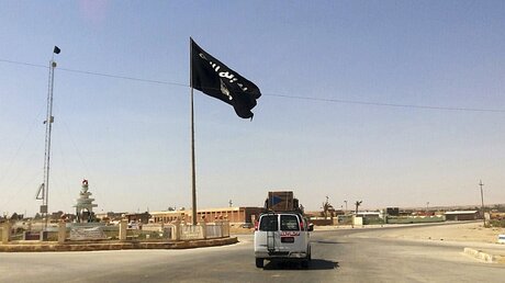 Ein Kleintransporter fährt an einer IS-Flagge vorbei / © N.N. (dpa)