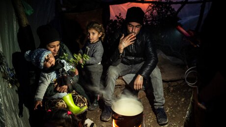 Eine Flüchtlingsfamilie bereitet ihr Essen über einem offenen Feuer in einem Flüchtlingslager auf Samos zu / © Angelos Tzortzinis (dpa)