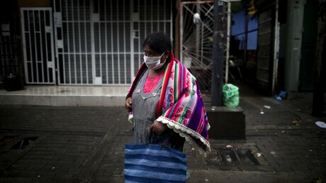 Eine Frau mit Mundschutz geht im Slum in Buenos Aires über die Straße / © Natacha Pisarenko (dpa)