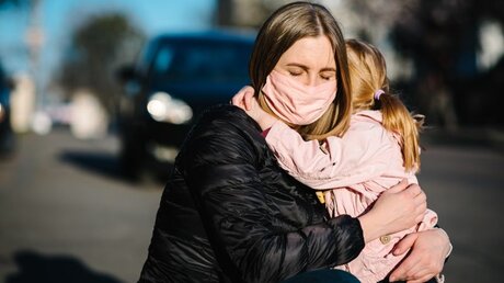Eine Frau mit Schutzmaske umarmt ihre Tochter / © Sergii Sobolevskyi (shutterstock)