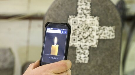 Eine Kerze erscheint auf dem Bildschirm des Smartphones, nachdem der QR-Code mittels einer App eingescannt wurde.  / © Jörg Loeffke (KNA)