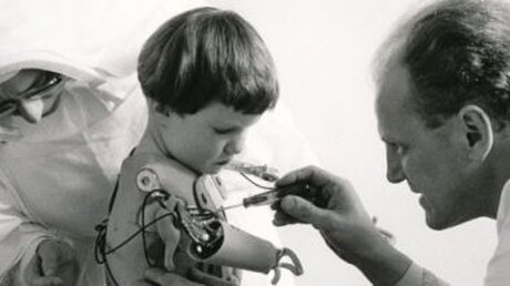 Eine Krankenschwester und ein Arzt passen einem contergangeschädigten Kind Armprothesen an / © Ernst Herb (KNA)
