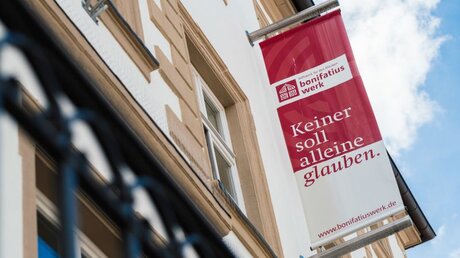 Fahne mit der Aufschrift "Keiner soll alleine glauben" am Hauptsitz des Bonifatiuswerkes in Paderborn / © Andreas Kühlken (KNA)