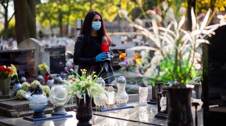 Frau mit Mundschutz und Grablicht auf einem Friedhof / © lusia599 (shutterstock)