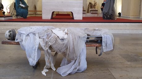 documenta: In weißem Tüll gehülltes Skelett auf einer Bahre in St. Kunigundis / © Birgitt Schippers (DR)