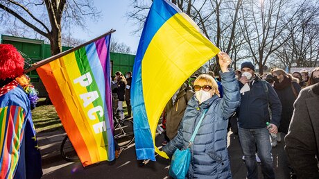 Eine Frau schwenkt die Nationalflagge der Ukraine bei einer Demonstration gegen den Krieg in der Ukraine am Rosenmontag, dem 28. Februar 2022 in Köln. Vor ihr weht eine Friedensfahne in Regenbogenfarben. / © Theodor Barth (KNA)