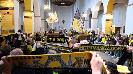 Fans von Borussia Dortmund halten beim Gottesdienst in der Gründungskirche des BVB ihre Fanschals in die Höhe / © Federico Gambarini (dpa)