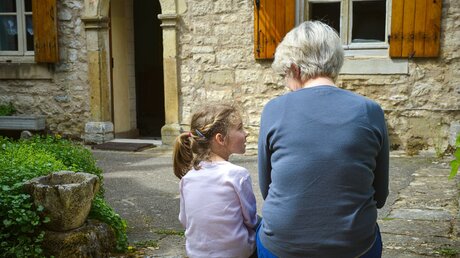 Ein kleines Mädchen sitzt am 23. April 2014 neben ihrer Großmutter auf dem Boden im Hof eines Hauses in Vezelay in Frankreich / © Corinne Simon (KNA)