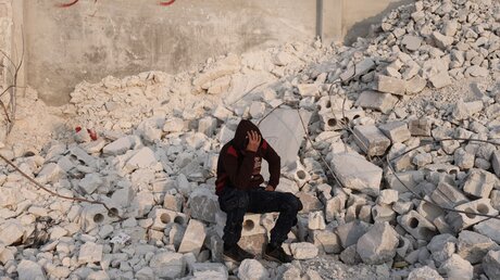 Syrien, Al Atarib: Ein Junge sitzt in der Nähe seines zerstörten Hauses, das durch das Erdbeben an der türkisch-syrischen Grenze zerstört wurde. / © Anas Alkharboutli (dpa)