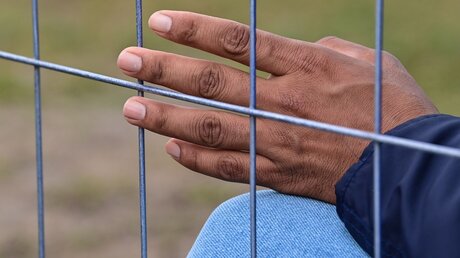 20.10.2021, Brandenburg, Eisenhüttenstadt: Die Hand eines Flüchtlings ist an einem Zaun der Zentralen Erstaufnahmeeinrichtung für Asylbewerber (ZABH) des Landes Brandenburg zu sehen. / © Patrick Pleul (dpa)