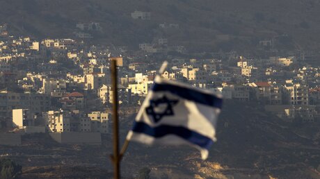 Blick auf eine israelische Flagge vor einem Dorf / © Ariel Schalit (dpa)