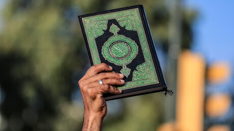 Ein Mann hält ein Exemplar des Koran während eines Protests in Irak nach der Koranverbrennung in Schweden / © Ameer Al-Mohammedawi (dpa)