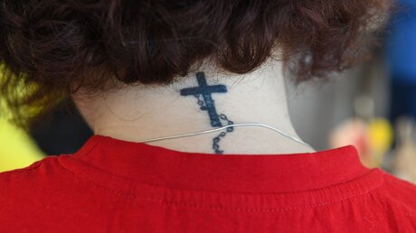 Eine Frau trägt im Nacken ein Tattoo mit der Darstellung eines Kreuzes und einem Rosenkranz / © Harald Oppitz (KNA)