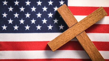 Ein Holzkreuz liegt auf einer US-amerikanischen Fahne / © Julia Steinbrecht (KNA)